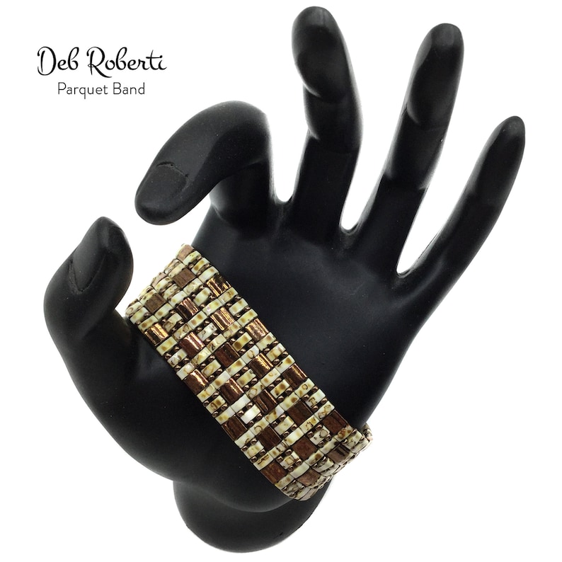 May include: A brown and white beaded bracelet with a parquet pattern. The bracelet is on a black hand model. The text "Deb Roberti Parquet Band" is visible above the bracelet.