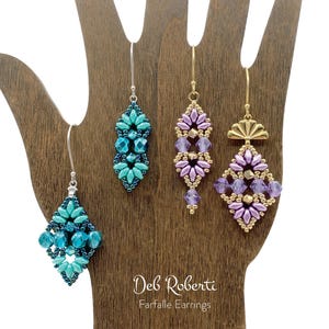 May include: Three pairs of handmade earrings displayed on a wooden hand. The earrings are made with beads in shades of teal, purple, and gold. The earrings are labeled "Deb Roberta Farfalle Earrings".