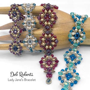 Könnte beinhalten: Vier Armbänder mit Perlen in Lila, Blau und Türkis. Die Armbänder sind aus kleinen Perlen und Kristallen gefertigt und werden auf einer Holzhand präsentiert. Der Text "Deb Roberti Lady Jane's Bracelet" steht unten.