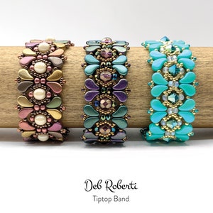 Op de afbeelding: Drie kralenarmbanden met een bloemenpatroon. De armbanden zijn in tinten goud, paars en turquoise.