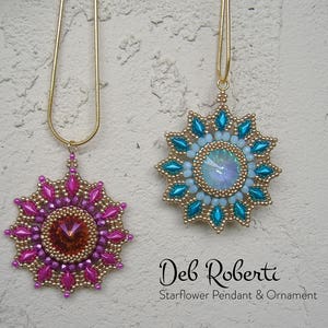 May include: Two gold chain necklaces with starburst pendants. The pendant on the left is pink and gold with a clear crystal in the center. The pendant on the right is blue and gold with a clear iridescent crystal in the center. The text "Deb Roberta Starflower Pendant & Ornament" is below the pendants.