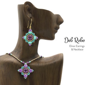 Pode incluir: Um conjunto de colar e brincos de ouro com um pingente e brincos de contas roxas e turquesa em forma quadrada. As joias são exibidas em um manequim de madeira. O texto "Deb Roberti Elinor Earrings & Necklace" é visível na imagem.