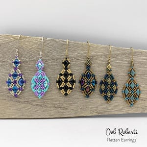 Puede incluir: Seis pares de pendientes de ratán con cuentas en varios colores, incluyendo azul, morado, negro y dorado. Cada pendiente presenta un diseño en forma de diamante con intrincados abalorios y un gancho de metal. Los pendientes se exhiben sobre una superficie de madera.