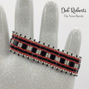 May include: A red, black, and silver beaded bracelet with a geometric pattern. The bracelet is made by Deb Roberti and is called a Tila Time Band.