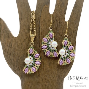 Puede incluir: Un conjunto de pendientes de oro y un collar con un colgante en forma de media luna. Las joyas están hechas con cuentas moradas y verdes y tienen un acento de perla.