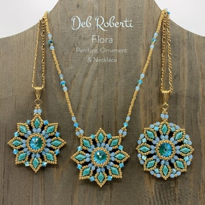 May include: A gold chain necklace with a blue and green beaded pendant in the shape of a flower. The pendant is a large, intricate design with a crystal in the centre. The necklace is displayed on a wooden background with the text "Deb Roberti Flora Pendant Ornament & Necklace".