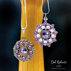 Op de afbeelding: Twee kralen hangers, een met een paars en groen ontwerp en de andere met een paars en wit ontwerp, beide met een zilveren ketting en een kristal in het midden. De hangers hangen aan een houten oppervlak. De tekst "Deb Roberti Juliet Pendant & Ornament" staat onder de hangers.