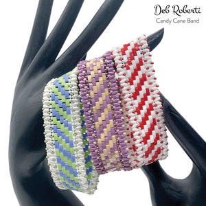 Puede incluir: Cuatro pulseras de cuentas con un patrón de bastón de caramelo. Las pulseras son de color rojo y blanco, morado y crema, crema y amarillo y verde y blanco.