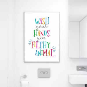 May include: A rectangular wall art print featuring the text WASH your HANDS you FILTHY ANIMAL in colorful, multi-colored lettering. The words are stacked vertically with a playful font style, set against a plain white background.