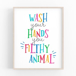 May include: A framed wall art print featuring the text WASH your HANDS you FILTHY ANIMAL in a variety of bright, multicolored letters. The words are arranged in a vertical layout with decorative lines accenting the text on a white background.