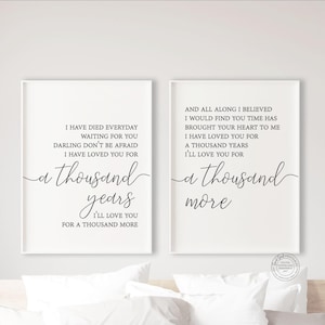 Può includere: Due stampe incorniciate con testi di canzoni romantiche in scrittura nera. La prima stampa recita "a thousand years" e la seconda "a thousand more". Le stampe sono esposte sopra un letto con biancheria da letto bianca.