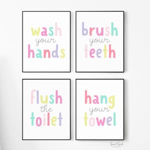 May include: Four framed bathroom art prints with black borders. Each print features a different instruction in colorful bubble letters: "wash your hands," "brush your teeth," "flush the toilet," and "hang your towel."