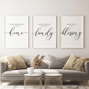 May include: Three white framed prints with black calligraphy text. The first print says "Having somewhere to go is home". The second print says "Having someone to love is family". The third print says "Having both is a blessing".