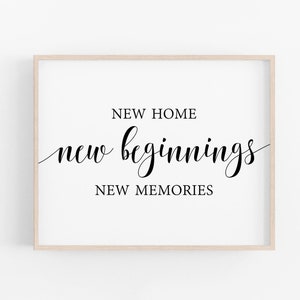 Puede incluir: Una impresión enmarcada con el texto "NEW HOME new beginnings NEW MEMORIES" en fuente cursiva negra sobre un fondo blanco.