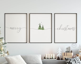 May include: Three framed art prints with black frames. The left print says "merry" in cursive. The center print has two green Christmas trees. The right print says "christmas" in cursive. The prints are displayed above a gray sofa.