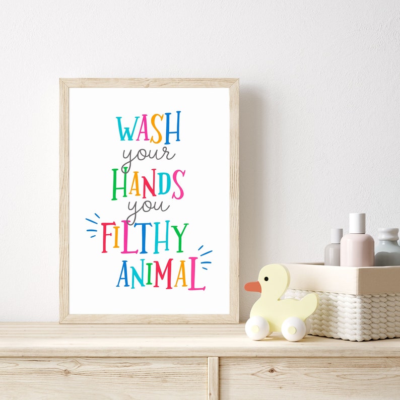 May include: A rectangular framed wall art print featuring the text WASH your HANDS you FILTHY ANIMAL in a variety of bright, multi-colored letters. The frame is made of light-colored wood and the background of the print is solid white.