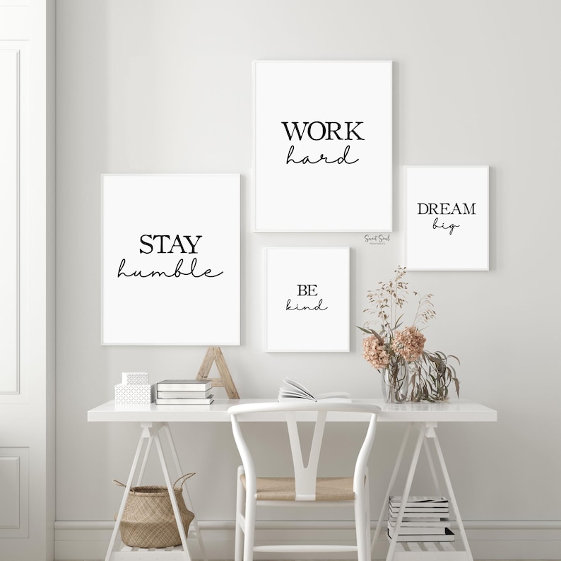 May include: Four framed wall art prints with motivational quotes in black script on white backgrounds. The quotes read "WORK hard", "STAY humble", "BE kind", and "DREAM big". The prints are displayed above a white desk with a chair and decorative items.