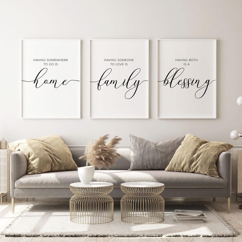 May include: Three white framed prints with black calligraphy text. The first print says "Having somewhere to go is home". The second print says "Having someone to love is family". The third print says "Having both is a blessing".