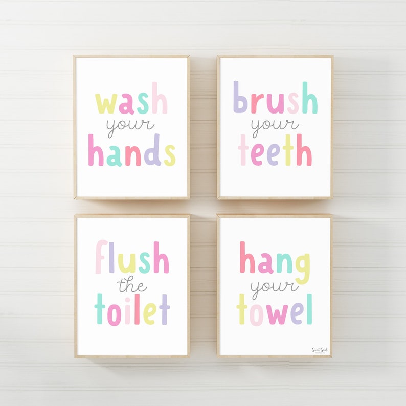 May include: Four framed prints with white backgrounds and pastel-colored text. The prints read "wash your hands," "brush your teeth," "flush the toilet," and "hang your towel." The frames are a light wood color, and the text is in a playful font.
