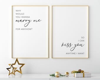 Puede incluir: Dos láminas de pared verticales en marcos dorados finos. La lámina izquierda dice: WHY WOULD YOU WANNA marry me FOR ANYHOW? La derecha dice: SO I CAN kiss you ANYTIME I WANT. Texto negro sobre fondo blanco con fuentes manuscritas y sans-serif.