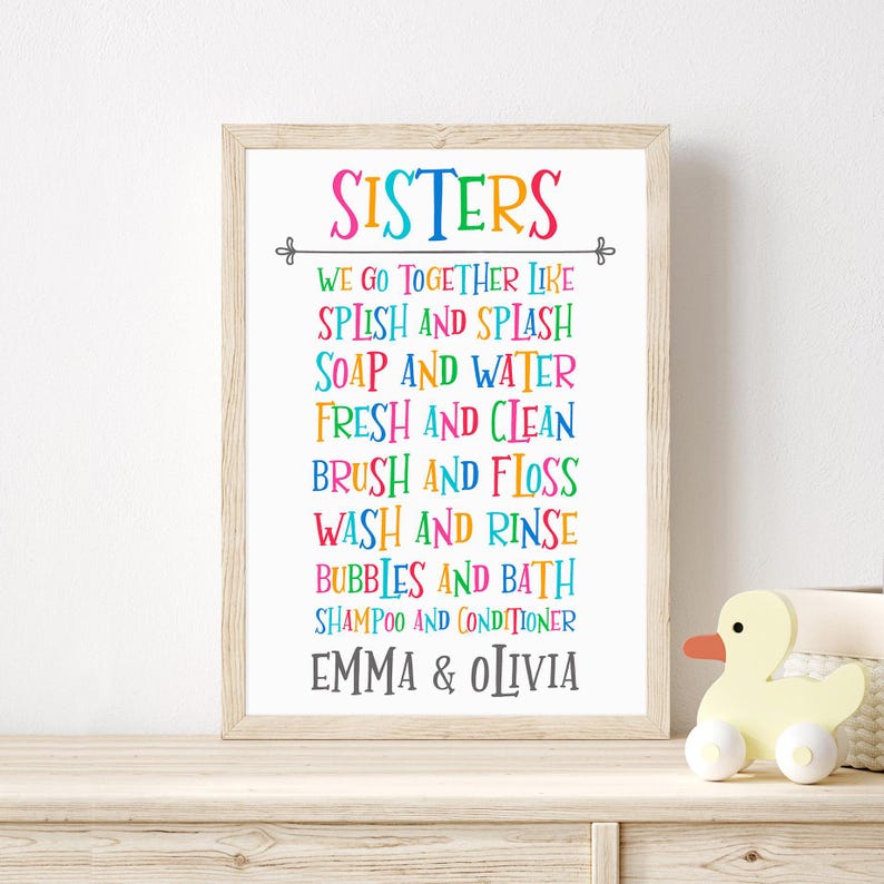 May include: A colorful framed print with the text "SISTERS" and a list of rhyming phrases about things sisters do together, such as "Splish and Splash" and "Soap and Water". The names "Emma & Olivia" are at the bottom of the print.