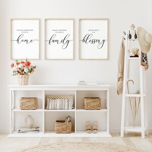 May include: Three framed prints with white backgrounds and black calligraphy text. The prints are hung on a white wall. The text on the prints reads "Having somewhere to go is home", "Having someone to love is family", and "Having both is a blessing".