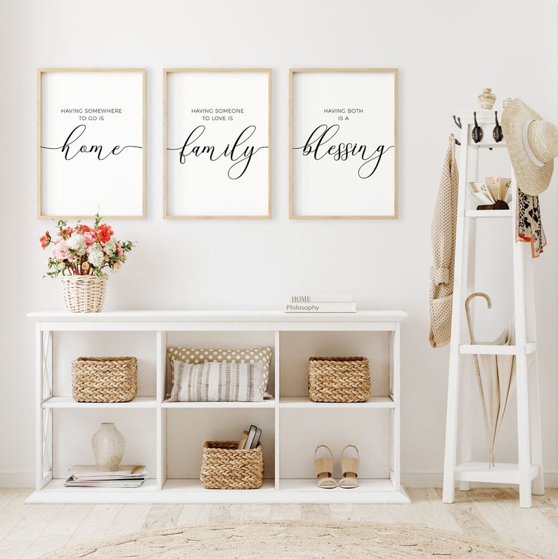 May include: Three framed prints with white backgrounds and black calligraphy text. The prints are hung on a white wall. The text on the prints reads "Having somewhere to go is home", "Having someone to love is family", and "Having both is a blessing".