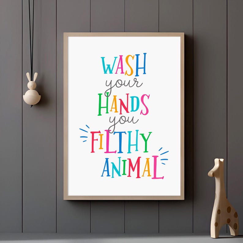 May include: A rectangular wall art print in a light wood frame featuring the colorful text WASH your HANDS you FILTHY ANIMAL. The words are written in a mix of blue, orange, green, pink, and yellow fonts against a plain white background.