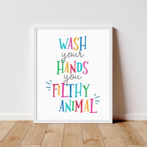 May include: A white framed wall art print featuring the multicolored text WASH your HANDS you FILTHY ANIMAL. The words are displayed in a variety of bright colors including blue, orange, green, pink, and yellow, set against a plain white background.