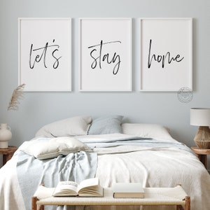 Pu&ograve; includere: Tre stampe incorniciate bianche con testo in calligrafia nera. Le stampe recitano "let's", "stay" e "home". Le stampe sono appese a un muro blu chiaro sopra un letto con biancheria da letto bianca.