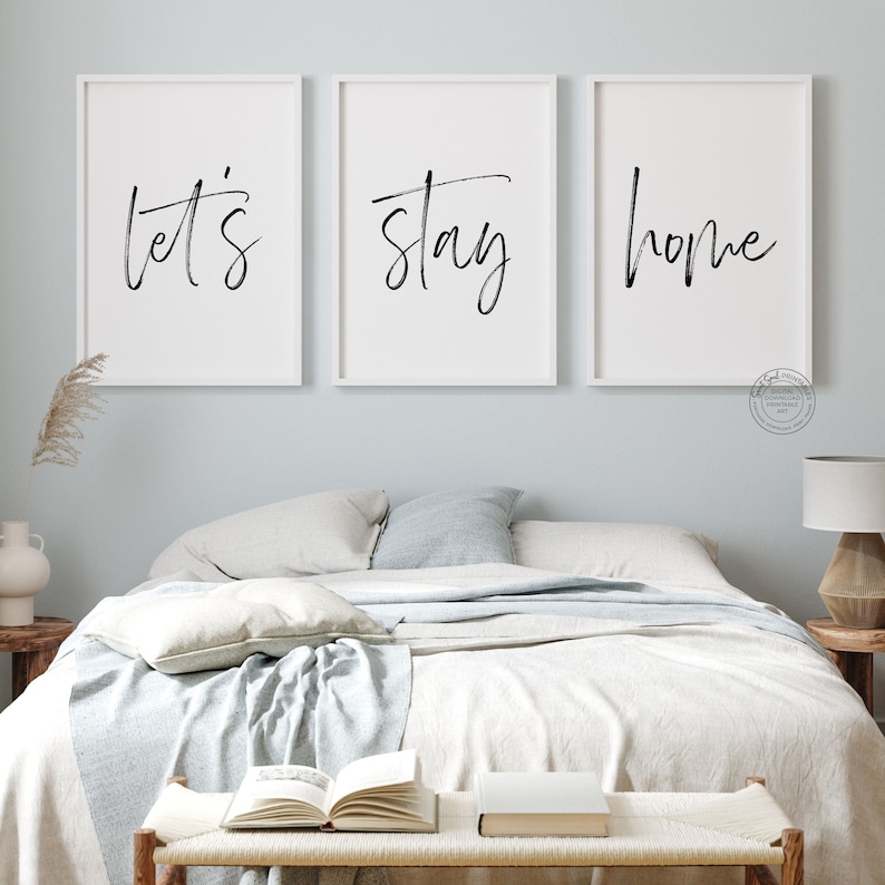 Pu&ograve; includere: Tre stampe incorniciate bianche con testo in calligrafia nera. Le stampe recitano "let's", "stay" e "home". Le stampe sono appese a un muro blu chiaro sopra un letto con biancheria da letto bianca.