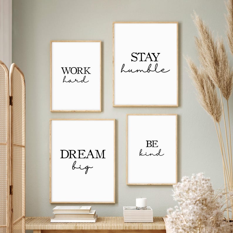 May include: Four framed art prints with motivational quotes. The prints feature the phrases "WORK hard", "STAY humble", "DREAM big", and "BE kind" in black script on a white background, set in light wood frames.