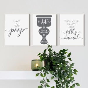 May include: A set of three rectangular wall art prints with white backgrounds and dark gray text. The left print reads Have a Nice Poop, the center print features a toilet graphic with the text Shit is About to Go Down, and the right print reads Wash Your Hands You Filthy Animal.