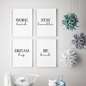 May include: Four framed white prints with black text that reads "WORK hard", "STAY humble", "DREAM big", and "BE kind". Decorative hanging paper pom-poms in shades of green, gray, and white are suspended from the ceiling.