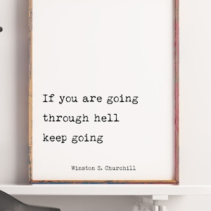 Puede incluir: Una cita motivacional enmarcada de Winston S. Churchill que dice "Si estás pasando por el infierno, sigue adelante". La cita se muestra en una pared blanca sobre un escritorio blanco con una silla negra y un jarrón con ramas secas.