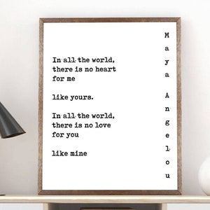 May include: A framed black and white typography print with the text 'In all the world, there is no heart for me like yours. In all the world, there is no love for you like mine.' The print is hanging on a white wall above a wooden desk with a white drawer and a black lamp. A white vase with a branch is on the right side of the desk. A black stool is in front of the desk.