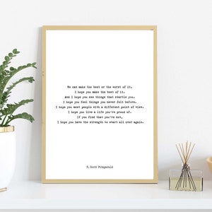 May include: A rectangular wall art print in a thin gold frame featuring black typewriter-style text on a white background. The quote reads: We can make the best or the worst of it. I hope you make the best of it. And I hope you see things that startle you. I hope you feel things you never felt before. I hope you meet people with a different point of view. I hope you live a life you're proud of. If you find that you're not, I hope you have the strength to start all over again. P. Scott Fitzgerald.