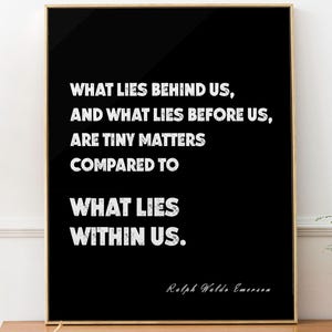 May include: A framed black and gold print featuring the quote "WHAT LIES BEHIND US, AND WHAT LIES BEFORE US, ARE TINY MATTERS COMPARED TO WHAT LIES WITHIN US." by Ralph Waldo Emerson. The print is displayed on a wooden cabinet.