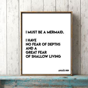 Może przedstawiać: Wydruk w ramie z białym tłem i czarnym tekstem, który brzmi: "Muszę być syreną. Nie boję się głębin i bardzo boję się płytkiego życia. Anaïs Nin."