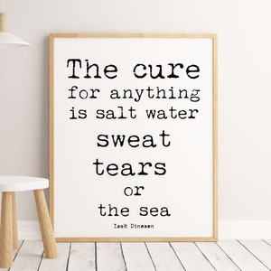 Pu&ograve; includere: Stampa incorniciata con la citazione "The cure for anything is salt water sweat tears or the sea" in testo nero su sfondo bianco. La cornice &egrave; marrone chiaro. Un piccolo sgabello bianco con gambe in legno &egrave; di fronte alla stampa.