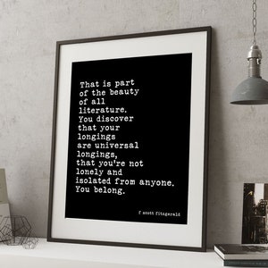 May include: A framed wall art print featuring a black background with white typewriter-style text that reads: That is part of the beauty of all literature. You discover that your longings are universal longings, that you're not lonely and isolated from anyone. You belong. F. Scott Fitzgerald.