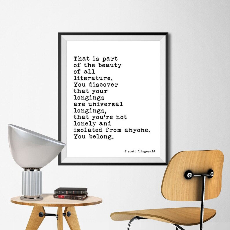 May include: A framed wall print featuring black typewriter-style text on a white background. The quote reads: That is part of the beauty of all literature. You discover that your longings are universal longings, that you're not lonely and isolated from anyone. You belong. F. Scott Fitzgerald.