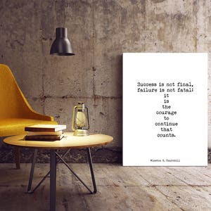May include: A motivational quote by Winston S. Churchill printed on a white canvas mounted on a wall. The quote reads: "Success is not final, failure is not fatal: it is the courage to continue that counts."