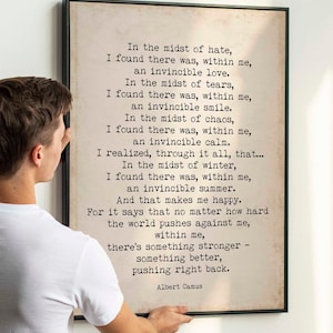 Op de afbeelding: Een ingelijst drukwerk met een beige achtergrond en zwarte tekst. De tekst is een citaat van Albert Camus over innerlijke kracht. Het citaat luidt: "Te midden van de haat, ontdekte ik dat er in mij een onoverwinnelijke liefde was. Te midden van de tranen, ontdekte ik dat er in mij een onoverwinnelijke glimlach was. Te midden van de chaos, ontdekte ik dat er in mij een onoverwinnelijke rust was. Ik realiseerde me, door het allemaal, dat... Te midden van de winter, ontdekte ik dat er in mij een onoverwinnelijke zomer was. En dat maakt me gelukkig. Want het zegt dat het niet uitmaakt hoe hard de wereld tegen me duwt, in mij is er iets sterkers - iets beters, dat terugduwt. - Albert Camus"