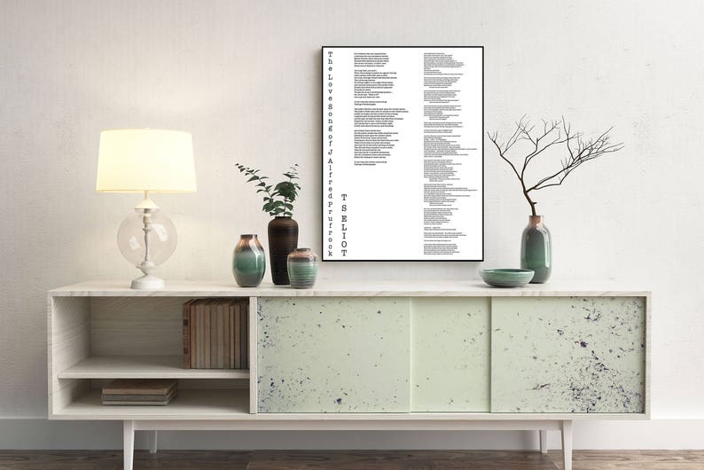 May include: A black and white framed print of a poem by T.S. Eliot, "The Love Song of J. Alfred Prufrock", hanging on a white wall above a light green cabinet with two doors. The cabinet has a shelf and is decorated with black speckles. There are two vases with green and brown flowers on the cabinet.