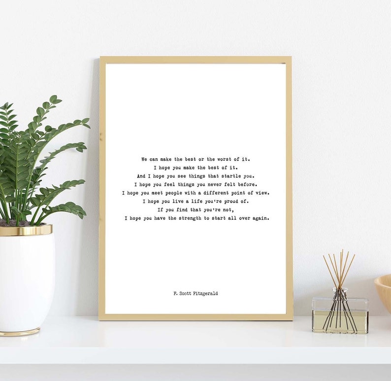 May include: A rectangular wall art print in a thin gold frame featuring black typewriter-style text on a white background. The quote reads: We can make the best or the worst of it. I hope you make the best of it. And I hope you see things that startle you. I hope you feel things you never felt before. I hope you meet people with a different point of view. I hope you live a life you're proud of. If you find that you're not, I hope you have the strength to start all over again. P. Scott Fitzgerald.