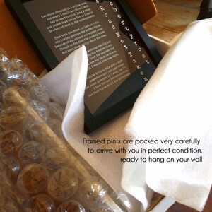 May include: A framed print of Robert Frost's poem "The Road Not Taken" with white text on a black background. The poem is surrounded by a white mat and a black frame. The print is packaged in a white box with bubble wrap for protection.