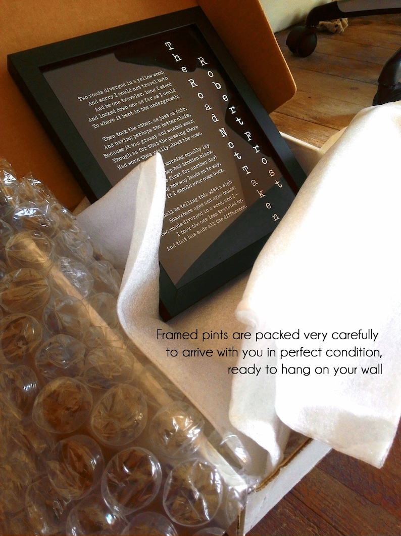 May include: A framed print of Robert Frost's poem "The Road Not Taken" with white text on a black background. The poem is surrounded by a white mat and a black frame. The print is packaged in a white box with bubble wrap for protection.