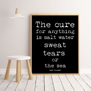 Pu&ograve; includere: Una stampa in bianco e nero incorniciata con la citazione "The cure for anything is salt water sweat tears or the sea" di Isak Dinesen. La stampa &egrave; esposta su una parete bianca accanto a un piccolo sgabello bianco con gambe in legno.