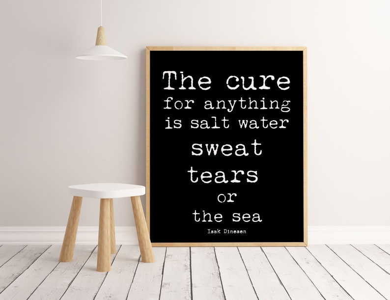 Pu&ograve; includere: Una stampa in bianco e nero incorniciata con la citazione "The cure for anything is salt water sweat tears or the sea" di Isak Dinesen. La stampa &egrave; esposta su una parete bianca accanto a un piccolo sgabello bianco con gambe in legno.